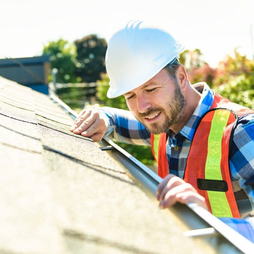 A man with hard hat standing on steps inspecting house roof