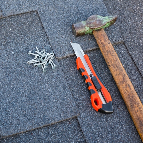 Close up view on asphalt bitumen shingles on a roof with hammer,nails and stationery knife background.